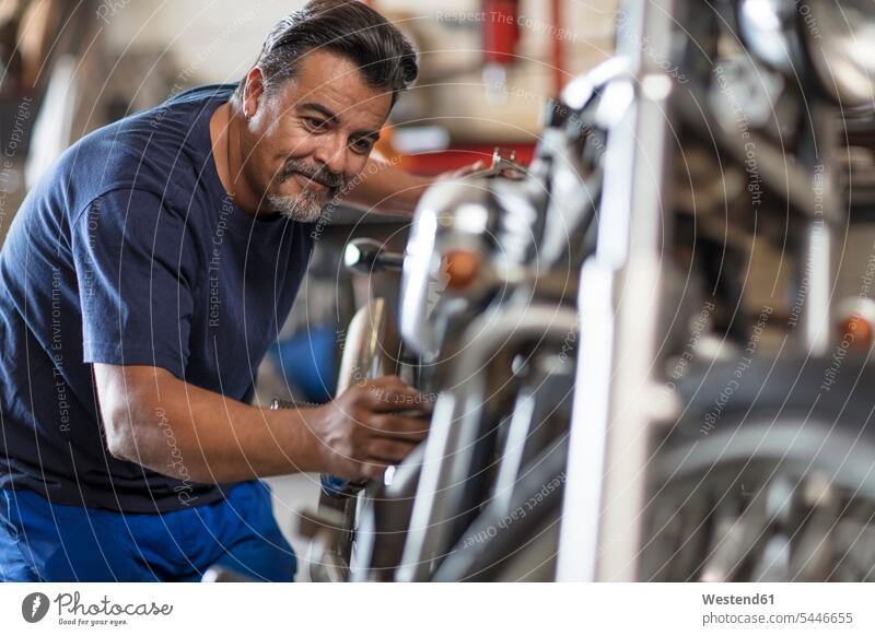 Selbstbewusster Mechaniker, der in der Werkstatt am Motorrad arbeitet arbeiten Arbeit lächeln reparieren Reparatur Motorräder Monteur Kraftfahrzeug