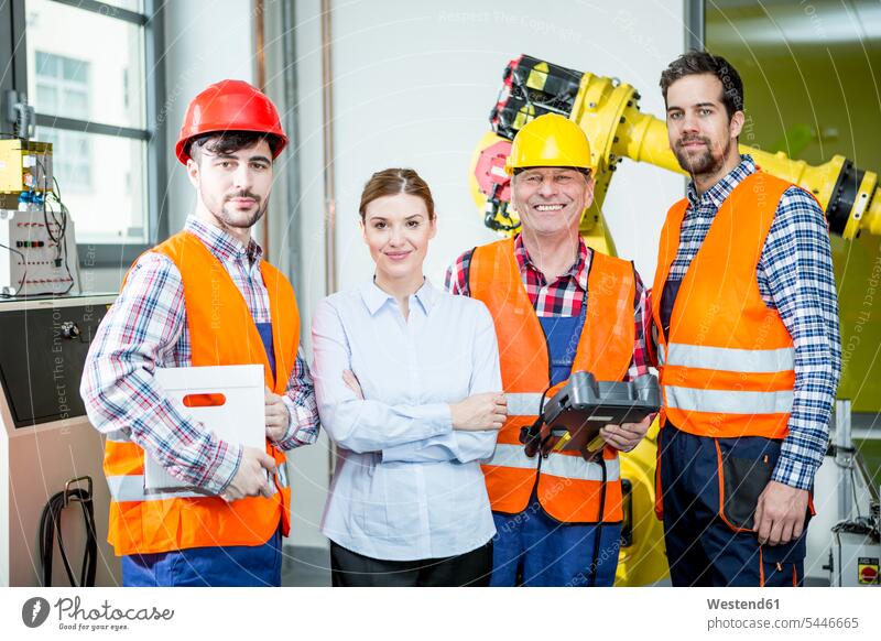 Porträt von selbstbewussten Mitarbeitern in einer Fabrik mit Industrieroboter im Hintergrund Roboter arbeiten Arbeit Fabriken lächeln industriell Gewerbe