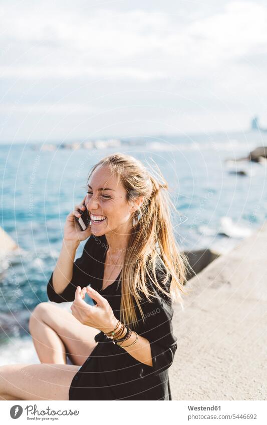 Glückliche junge Frau an der Strandpromenade am Handy telefonieren anrufen Anruf telephonieren lachen glücklich glücklich sein glücklichsein weiblich Frauen