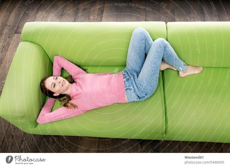 Lächelnde junge Frau auf der Couch liegend Sofa Couches Liege Sofas liegt Zuhause zu Hause daheim weiblich Frauen lächeln Erwachsener erwachsen Mensch Menschen