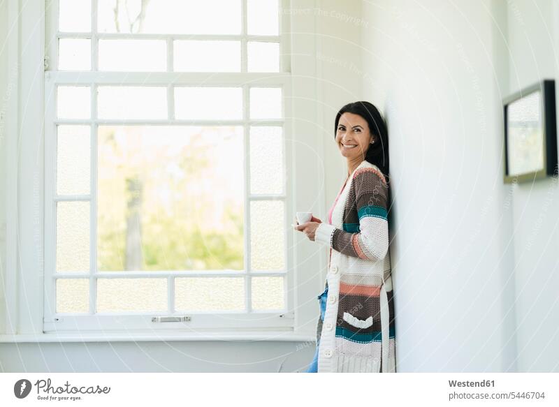 Porträt einer lächelnden Frau zu Hause stehen stehend steht entspannt entspanntheit relaxt weiblich Frauen Fenster Entspannung relaxen entspannen Erwachsener