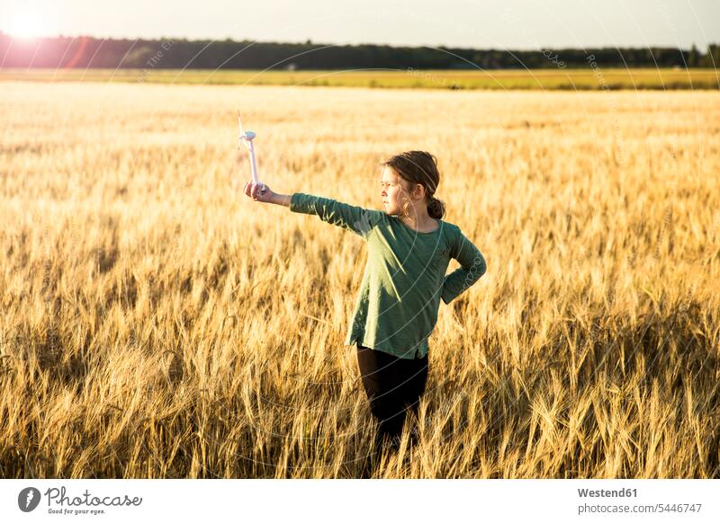 Mädchen steht im Getreidefeld und hält Miniatur-Windturbine halten Kornfeld Getreidefelder Kornfelder Windrad Windturbinen Windräder Feld Felder weiblich
