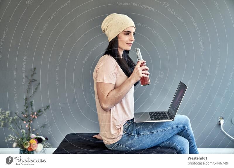 Junge Frau mit Laptop, die eine Flasche hält Notebook Laptops Notebooks sitzen sitzend sitzt Flaschen weiblich Frauen Computer Rechner Erwachsener erwachsen