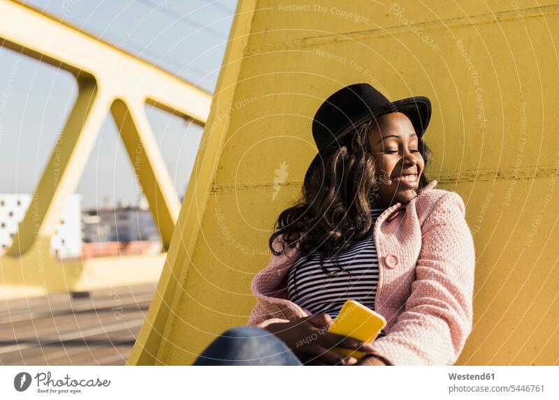 Junge Frau sitzt mit Smartphone auf der Brücke lachen Entspannung relaxen entspannen sitzen sitzend jung Bruecken Brücken weiblich Frauen fröhlich Fröhlichkeit