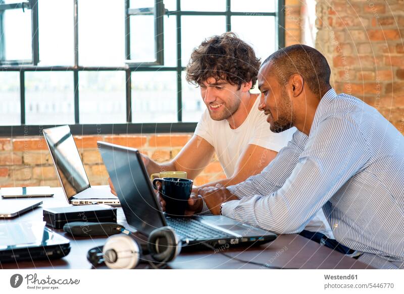 Zwei junge Geschäftsleute arbeiten in einem Arbeitsraum zusammen und benutzen Laptops Kollegen Arbeitskollegen Planung Pläne planen Coworking Space besprechen