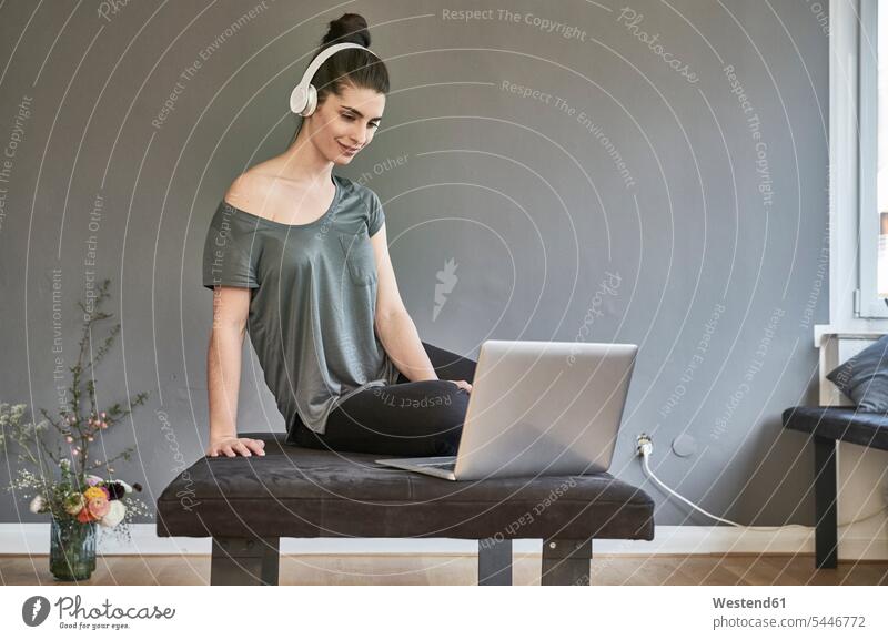 Junge Frau mit Kopfhörern sitzt mit Laptop im Wohnzimmer weiblich Frauen Notebook Laptops Notebooks Kopfhoerer Erwachsener erwachsen Mensch Menschen Leute