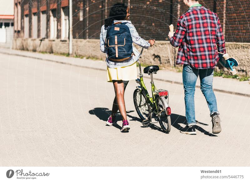 Junges Paar mit Fahrrad und Skateboard auf der Straße multikulturell gehen gehend geht Strassen Straßen jung Rollbretter Skateboards Pärchen Paare Partnerschaft