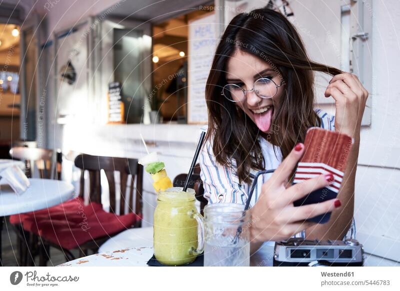 Junge Frau sitzt in einem Café und macht ein Selfie mit ihrem Smartphone fotografieren iPhone Smartphones Cafe Kaffeehaus Bistro Cafes Kaffeehäuser weiblich