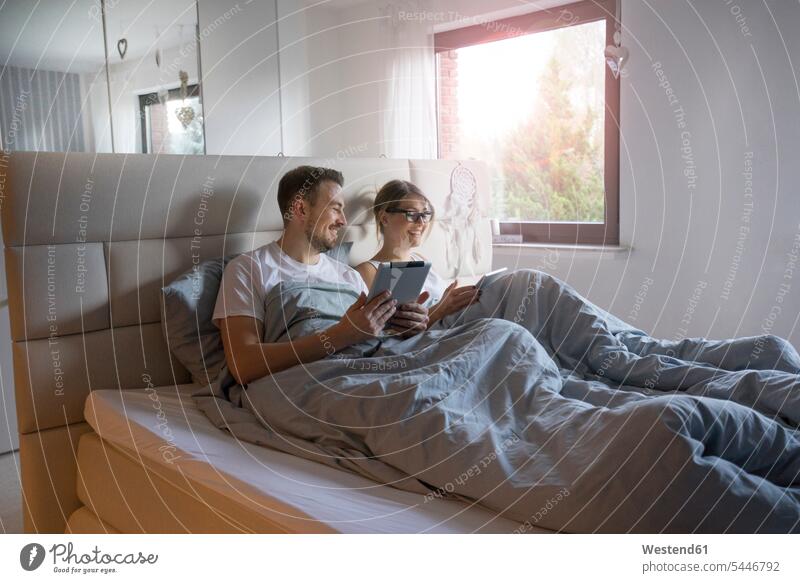 Lächelndes Paar zu Hause im Bett mit Tabletten Tablet Computer Tablet-PC Tablet PC iPad Tablet-Computer Zuhause daheim Pärchen Paare Partnerschaft Betten