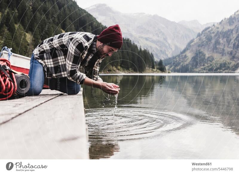Österreich, Tirol, Alpen, Mann kniet auf Steg und schöpft Wasser aus Bergsee Stege Anlegestelle Männer männlich See Seen Erwachsener erwachsen Mensch Menschen