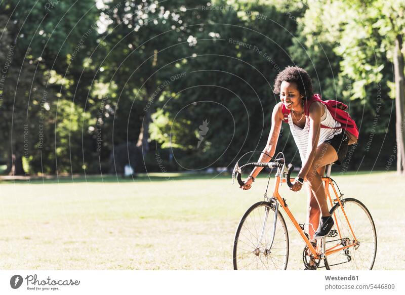 Lächelnde junge Frau fährt Fahrrad im Park Bikes Fahrräder Räder Rad weiblich Frauen Parkanlagen Parks lächeln fahren fahrend fahrender fahrendes Raeder