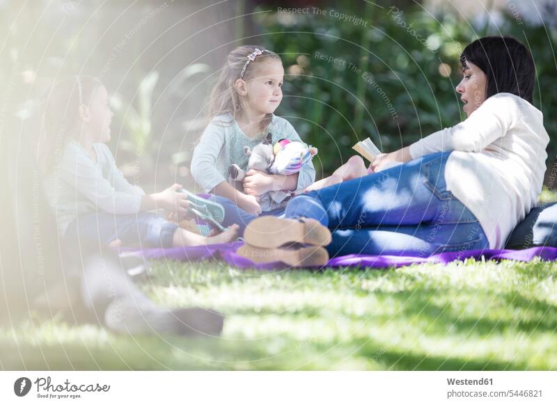 Mutter liest Kindern auf einer Picknickdecke ein Buch vor Familie lesen Tochter Mädchen Mensch Essen Eltern Wiese Natur Gras differenzierter Fokus Außenaufnahme