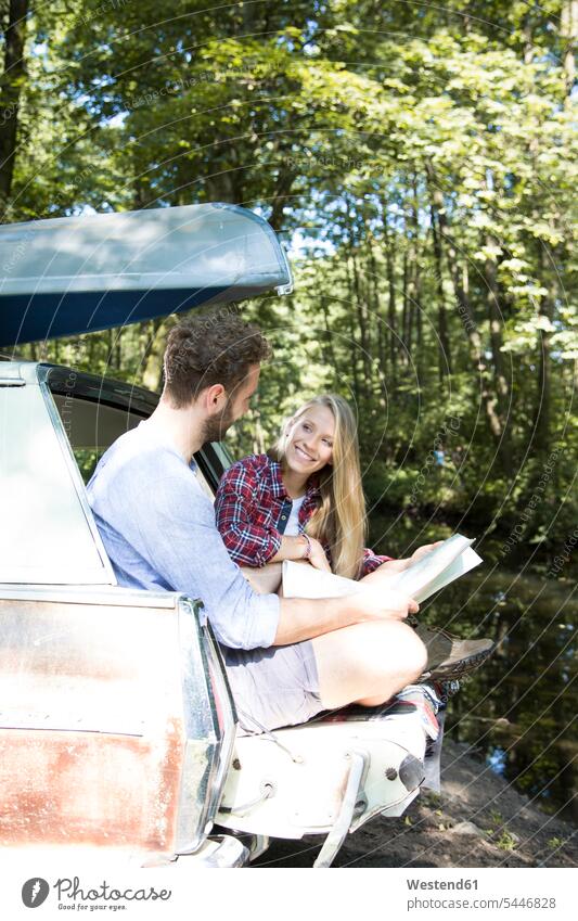 Lächelndes junges Paar mit Karte und Kanu im Auto an einem Bach Landkarte Landkarten Bäche Baeche Pärchen Paare Partnerschaft Wald Forst Wälder lächeln Wagen