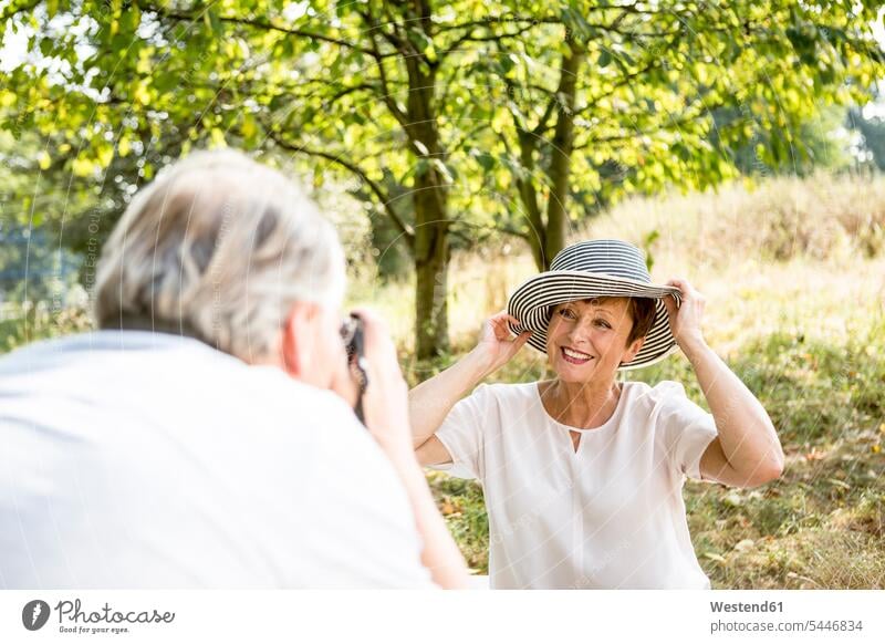 Älterer Mann fotografiert seine Frau auf der Wiese Wiesen Paar Pärchen Paare Partnerschaft lächeln fotografieren Fotoapparat Kamera Fotokamera Mensch Menschen