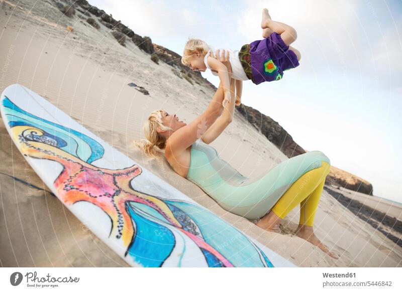 Spanien, Fuerteventura, glückliche Mutter und Tochter spielen am Strand neben dem Surfbrett Töchter Surfbretter surfboard surfboards Beach Straende Strände