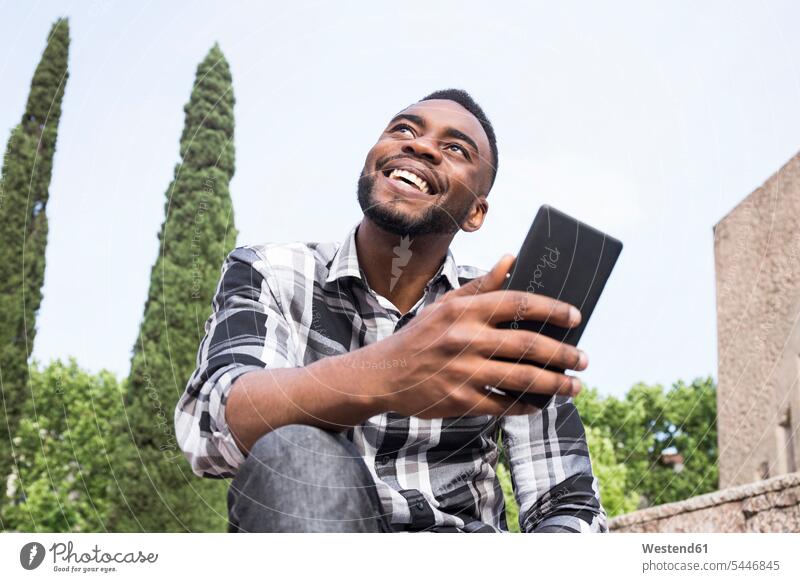 Porträt eines glücklichen jungen Mannes mit Handy Männer männlich Smartphone iPhone Smartphones Portrait Porträts Portraits Erwachsener erwachsen Mensch