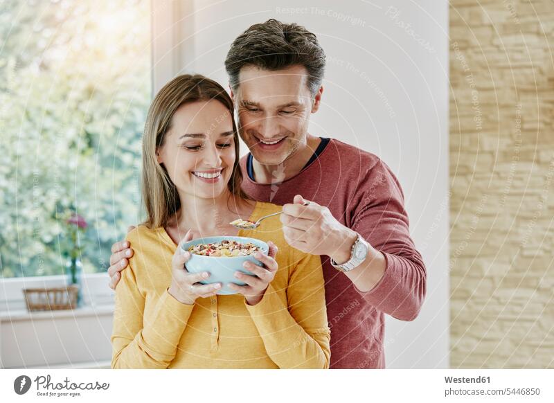 Glückliches Paar, das sich zu Hause ein Müsli teilt glücklich glücklich sein glücklichsein Portrait Porträts Portraits essen essend Pärchen Paare Partnerschaft