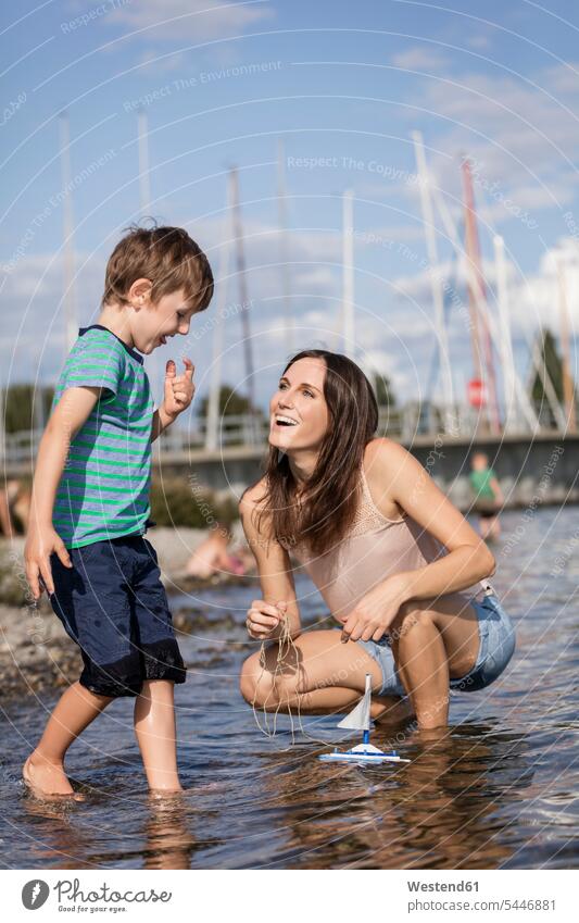 Deutschland, Friedrichshafen, Bodensee, glückliche Mutter und Sohn mit Spielzeugboot am Seeufer Söhne spielen Glück glücklich sein glücklichsein ansehen Mami