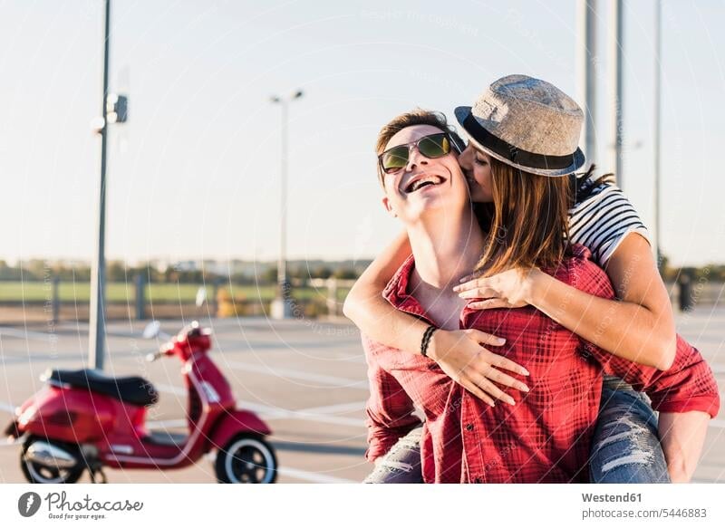 Glückliches junges Paar umarmt sich auf Parkebene mit einem Motorroller im Hintergrund Parkdeck Parkdecks umarmen Umarmung Umarmungen Arm umlegen Roller Piaggio