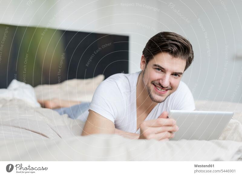 Porträt eines lächelnden Mannes, der mit einem Tablett auf dem Bett liegt Männer männlich Betten Erwachsener erwachsen Mensch Menschen Leute People Personen