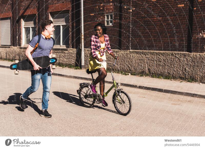 Junges Paar mit Fahrrad und Skateboard auf der Straße multikulturell jung Bikes Fahrräder Räder Rad flirten Flirt Rollbretter Skateboards fröhlich Fröhlichkeit