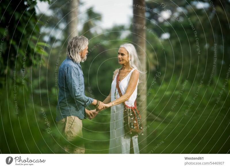 Liebenswertes älteres Ehepaar, das in tropischer Landschaft mit Palmen Händchen hält Natur unterwegs auf Achse in Bewegung Seniorenpaar älteres Paar