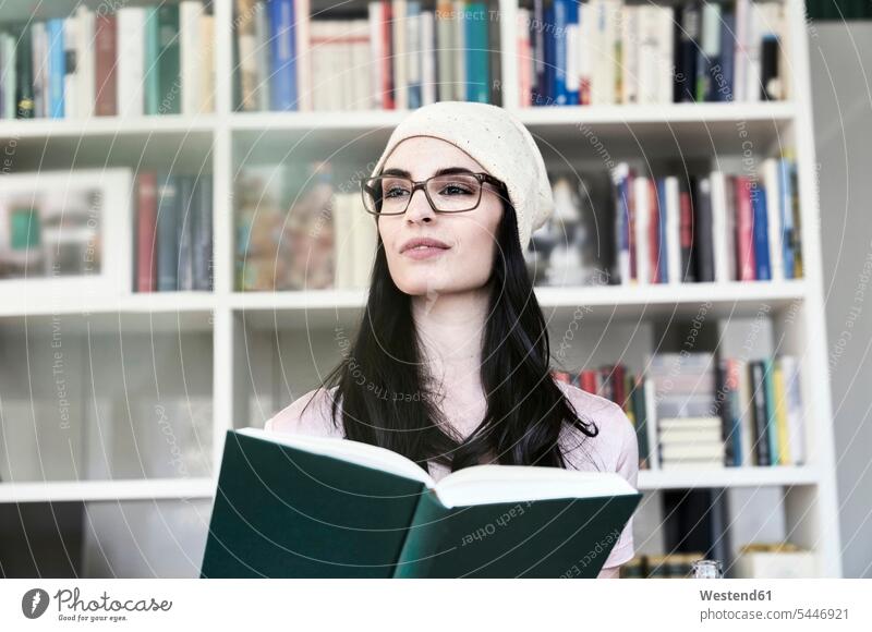 Junge Frau hält Buch und schaut zur Seite lesen Portrait Erwachsener Mensch Europäer Betrachtung Mütze Vorderansicht Beanie Wohnen Wohnung eine Person Style