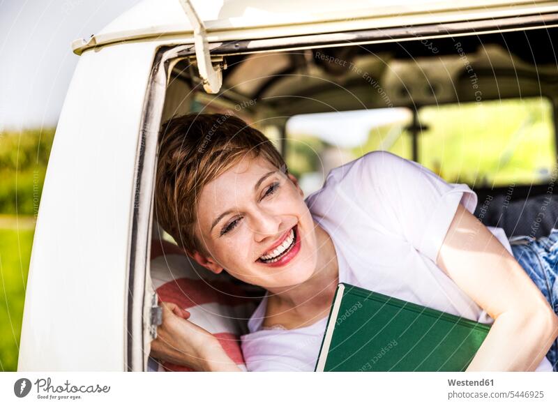 Glückliche Frau mit Buch in einem Lieferwagen lachen Kleinbus Kleinbusse weiblich Frauen Bücher positiv Emotion Gefühl Empfindung Emotionen Gefühle fühlen