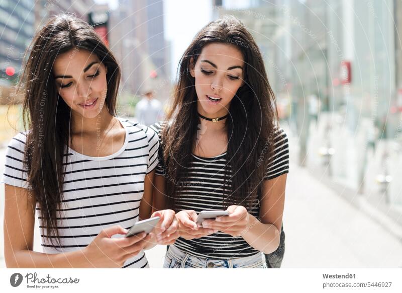 USA, New York City, zwei Zwillingsschwestern schauen sich in Manhattan Handys an Mobiltelefon Handies Mobiltelefone Schwester Schwestern Freundinnen