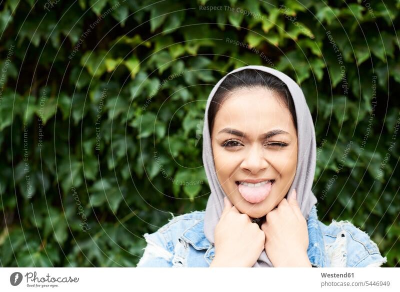 Porträt einer jungen Frau, die einen Hijab trägt und sich die Zunge herausstreckt Kopftuch Kopftücher muslimisch Moslem Muslim Zungen Portrait Porträts