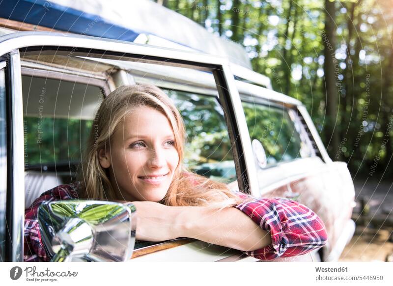 Lächelnde junge Frau im Auto im Wald weiblich Frauen Wagen PKWs Automobil Autos Forst Wälder lächeln Erwachsener erwachsen Mensch Menschen Leute People Personen