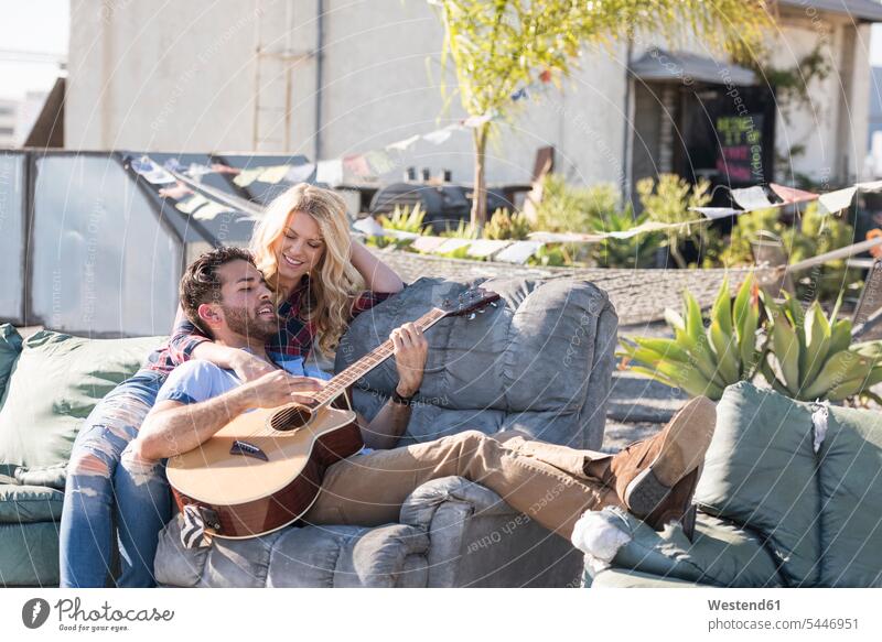 Auf dem Sofa sitzendes und Gitarre spielendes Paar auf einem Ropop singen Musiker fröhlich Fröhlichkeit Frohsinn Heiterkeit sitzt Gitarren Couches Liege Sofas