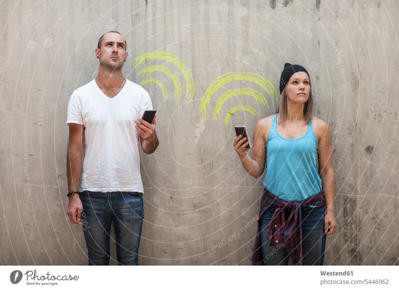 Mann und Frau halten ihre Telefone mit einem Wifi-Zeichen in Kreide Wand Wände Waende Symbol Symbole symbolisch Darstellung darstellen WLan Wireless Lan W-Lan