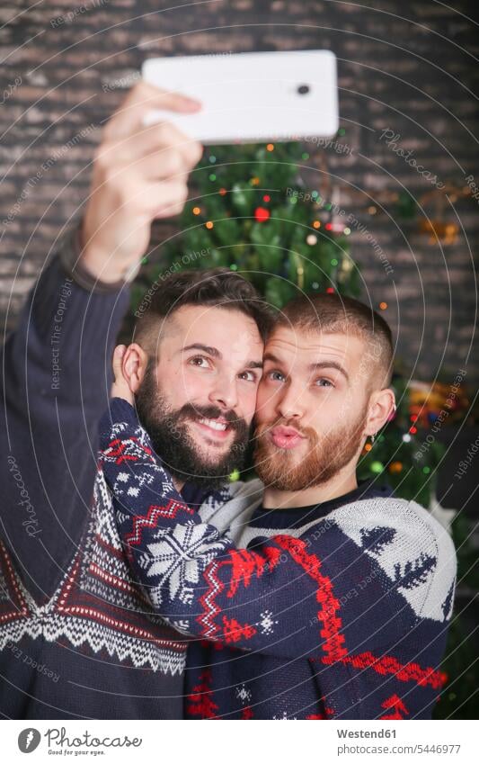 Porträt eines glücklichen schwulen Paares, das zu Weihnachten zu Hause ein Selfie mit dem Smartphone macht Portrait Porträts Portraits Selfies Schwules Paar