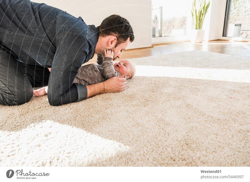 Vater und kleiner Sohn spielen zu Hause auf dem Teppich Zuhause daheim Papas Väter Vati Vatis Papis knuddeln umarmen lachen Kind Babies Babys Kinder Eltern