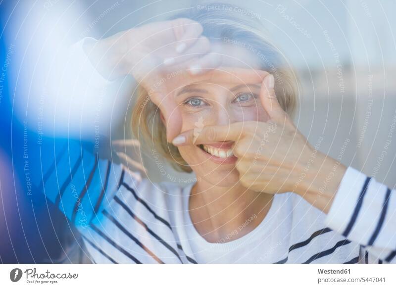 Porträt einer lachenden blonden Frau, die mit ihren Fingern einen Rahmen baut, während sie den Betrachter anschaut Portrait Porträts Portraits weiblich Frauen