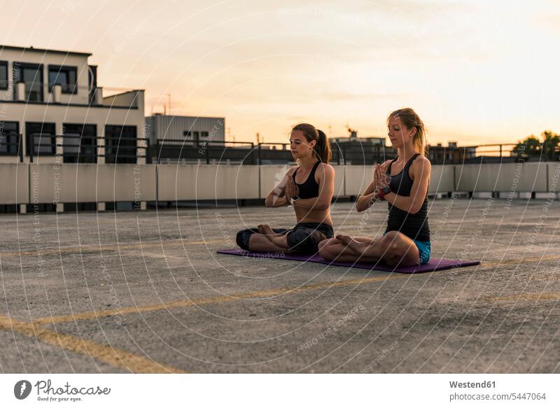 Zwei Frauen praktizieren Yoga auf einem Parkdeck in der Stadt Freundinnen sitzen sitzend sitzt weiblich Yoga-Übungen Yogauebungen Yogaübungen Jogauebung