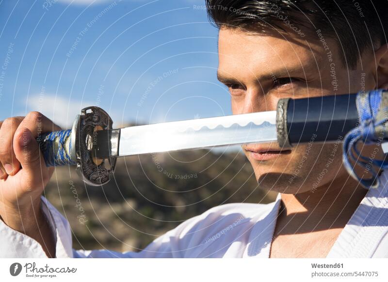 Mann mit trotzigen Augen zieht sein Katana-Schwert Männer männlich kämpfen kaempfen Schwerter Kampfsport Kampfsportart Kampfsportarten Kampfkunst Erwachsener