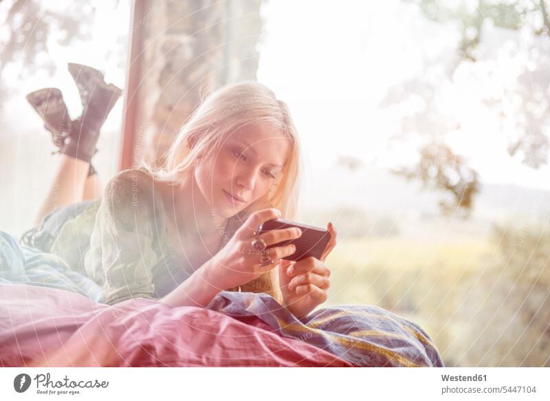 Porträt einer jungen Frau, die auf dem Bett liegt und auf ihr Handy schaut weiblich Frauen Smartphone iPhone Smartphones Erwachsener erwachsen Mensch Menschen