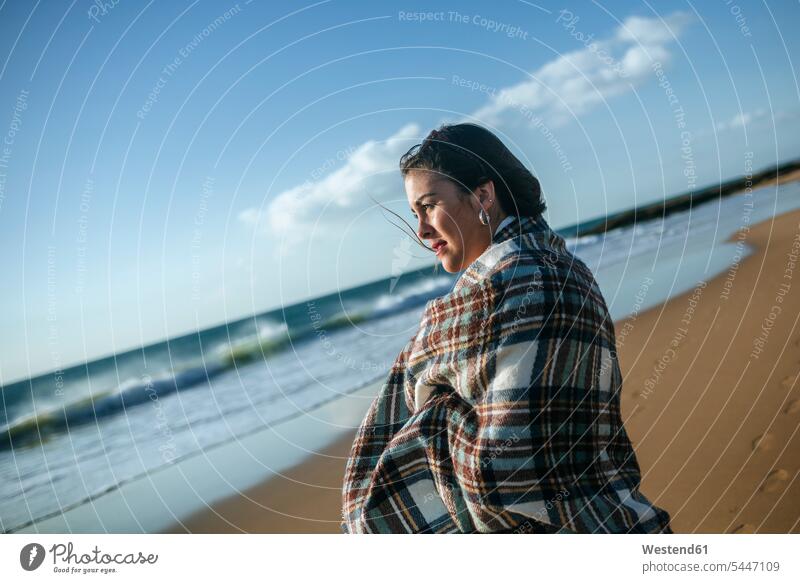 Junge Frau mit Decke am Strand mit Blick auf das Meer Beach Straende Strände Beaches weiblich Frauen Erwachsener erwachsen Mensch Menschen Leute People Personen