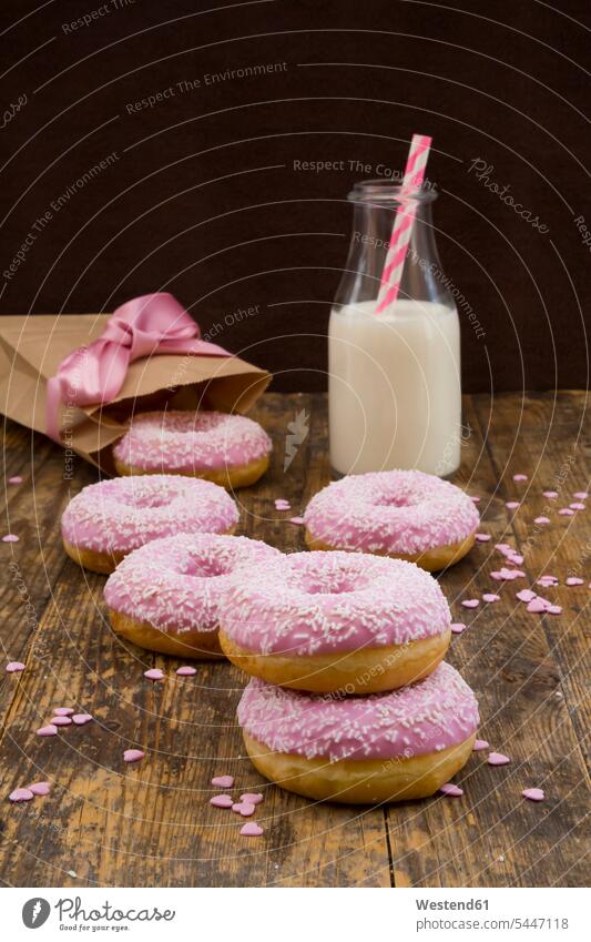 Doughnuts mit rosa Zuckerguss und Zuckergranulat und eine Flasche Milch auf Holz Schleife Schleifen hölzern rustikal übereinander obenauf aufeinander süß Süßes
