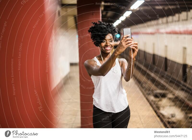 USA, New York City, Manhattan, lächelnde Frau, die ein Selfie am Bahnsteig einer U-Bahn-Station macht weiblich Frauen Selfies warten Smartphone iPhone