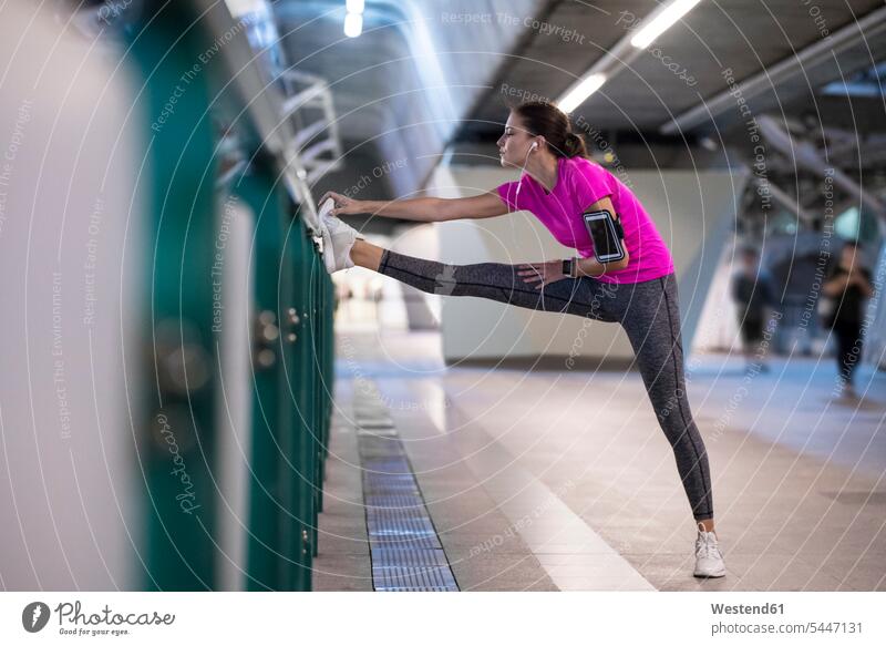 Junge Frau in rosa Sporthemd, die in der städtischen U-Bahn-Station Musik hört und sich streckt dehnen strecken junge Frau junge Frauen Joggerin Joggerinnen