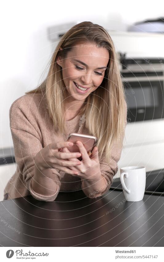 Porträt einer lächelnden blonden Frau, die zu Hause ein Mobiltelefon benutzt blonde Haare blondes Haar Smartphone iPhone Smartphones Zuhause daheim benutzen