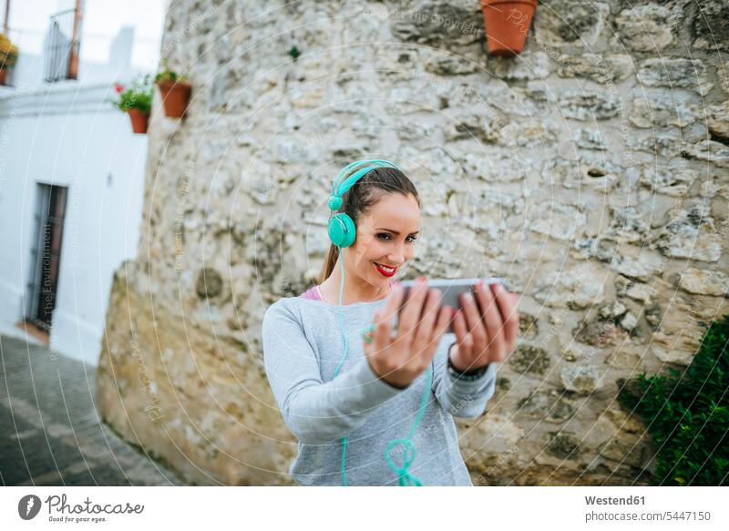 Junge Frau mit Kopfhörern macht Selfies Kopfhoerer Musik hören Smartphone iPhone Smartphones fotografieren jung weiblich Frauen Handy Mobiltelefon Handies