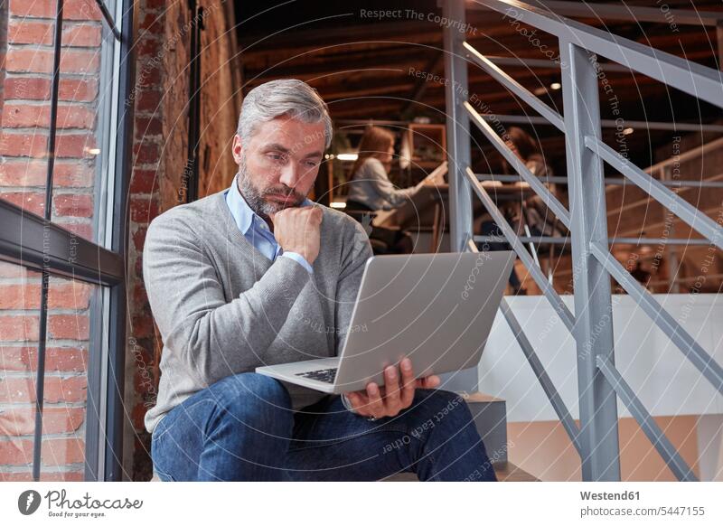 Geschäftsmann sitzt auf der Treppe eines modernen Büros und benutzt einen Laptop sitzen sitzend arbeiten Arbeit Office Loft Lofts Businessmann Businessmänner