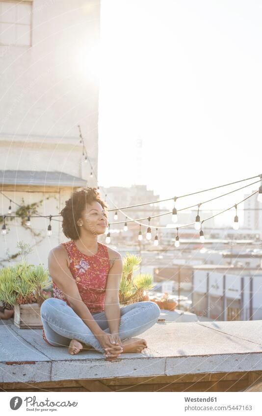 Junge Frau sitzt auf der Dachterrasse und genießt die Sonne Schneidersitz nachdenken überlegen sitzen sitzend Dachterrassen Entspannung relaxen entspannen