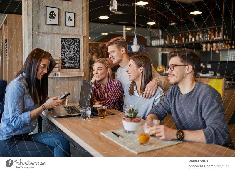 Gruppe von Freunden sitzt zusammen in einem Café mit Laptop, Smartphone und Getränken glücklich Glück glücklich sein glücklichsein Cafe Kaffeehaus Bistro Cafes