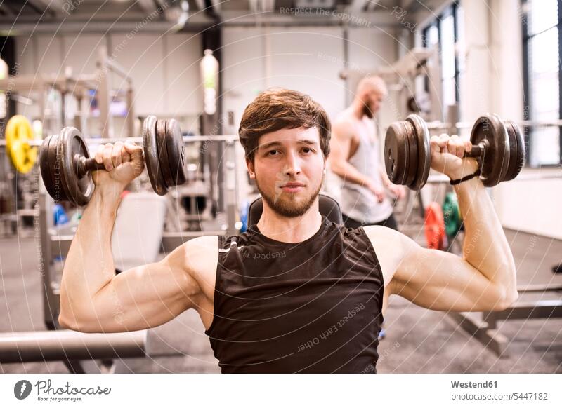 Junger Mann übt mit Hanteln im Fitnessstudio Gewichtheben junger Mann junge Männer Gewichte Gesundheit gesund trainieren fit Kraftsport Sport männlich