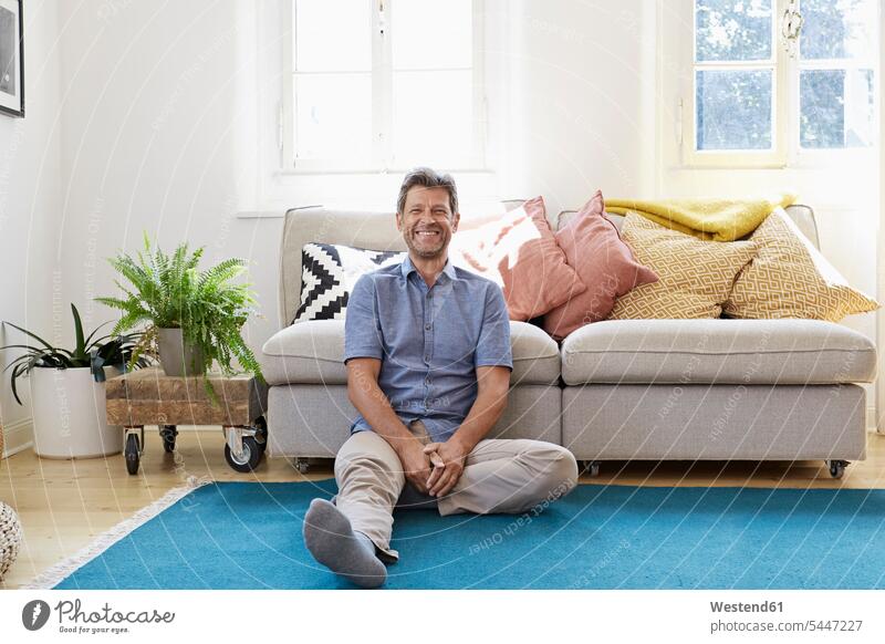 Mann sitzt zu Hause und sieht glücklich aus Männer männlich Boden Böden Boeden sitzen sitzend Entspannung entspannt Entspannen relaxen entspannen Zuhause daheim